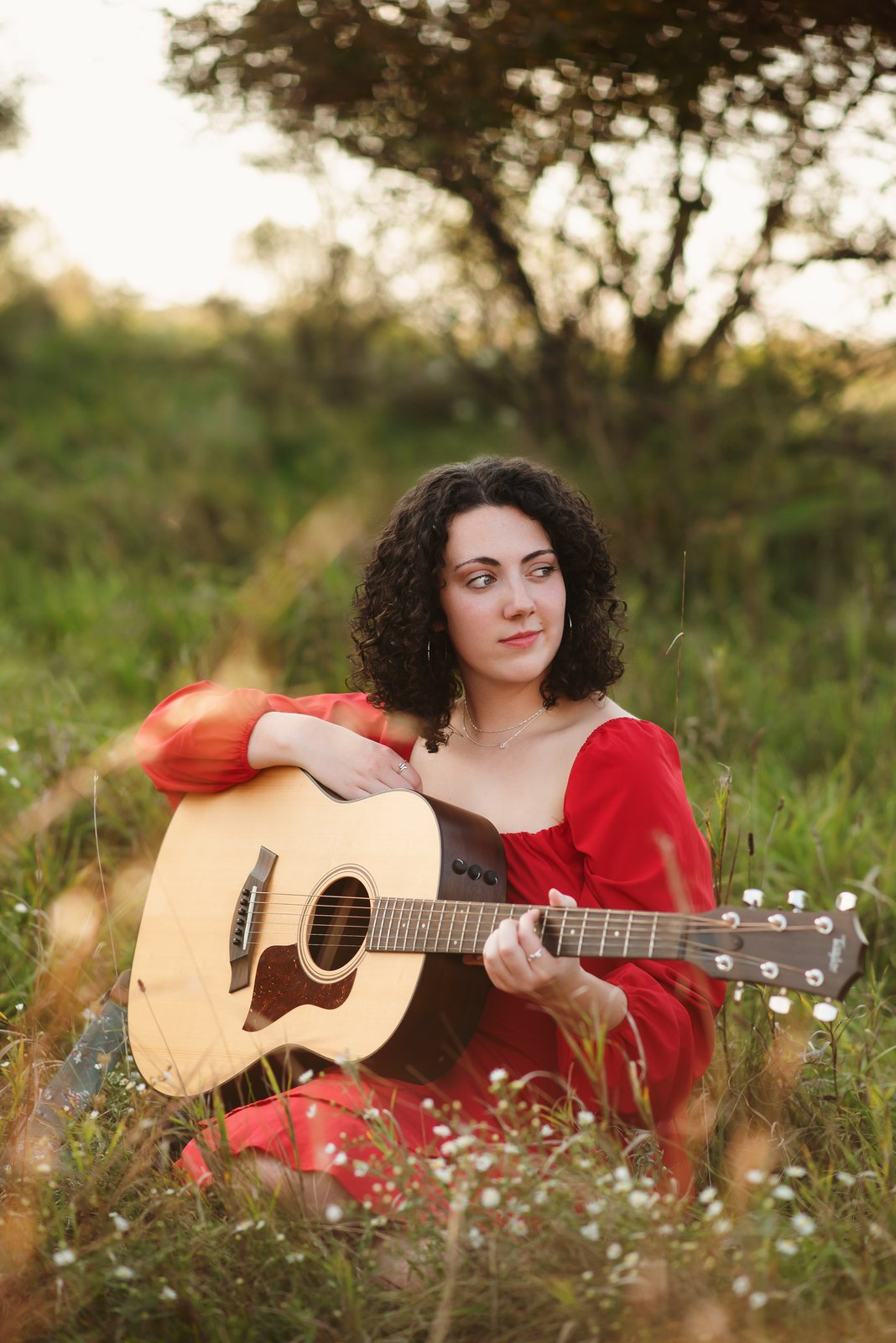 Gwendellyn Malee in a red dress holding her acoustic guitar in a wildflower field