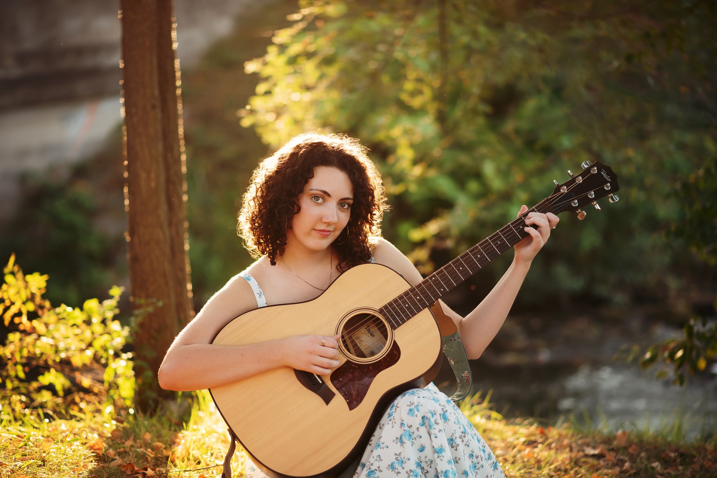 Gwendellyn Malee playing acoustic guitar by a creek at golden hour